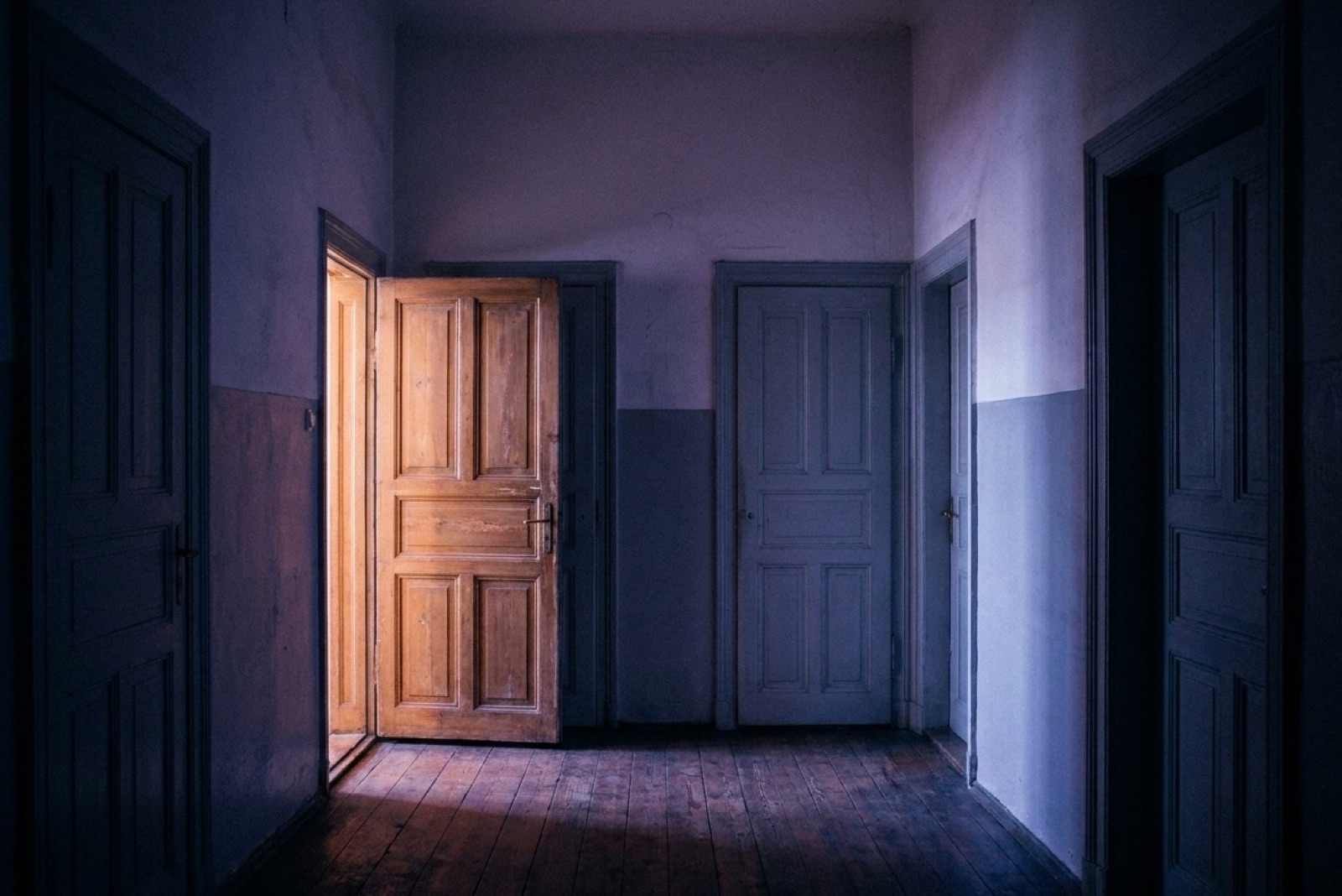 Flur eines Altbaus am Abend, eine Tür steht offen und warmes Licht fällt auf die Dielen