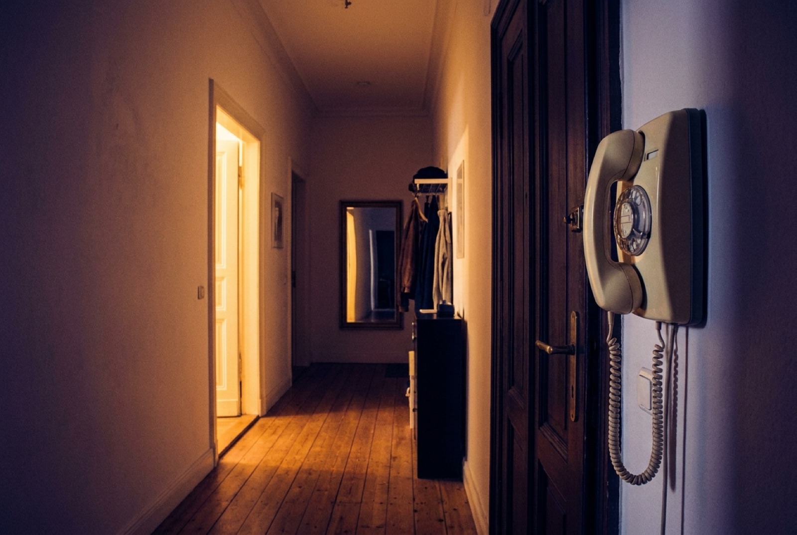 Wandtelefon im Hausflur eines Altbaus, warmes Licht aus einer angelehnten Wohnungstür