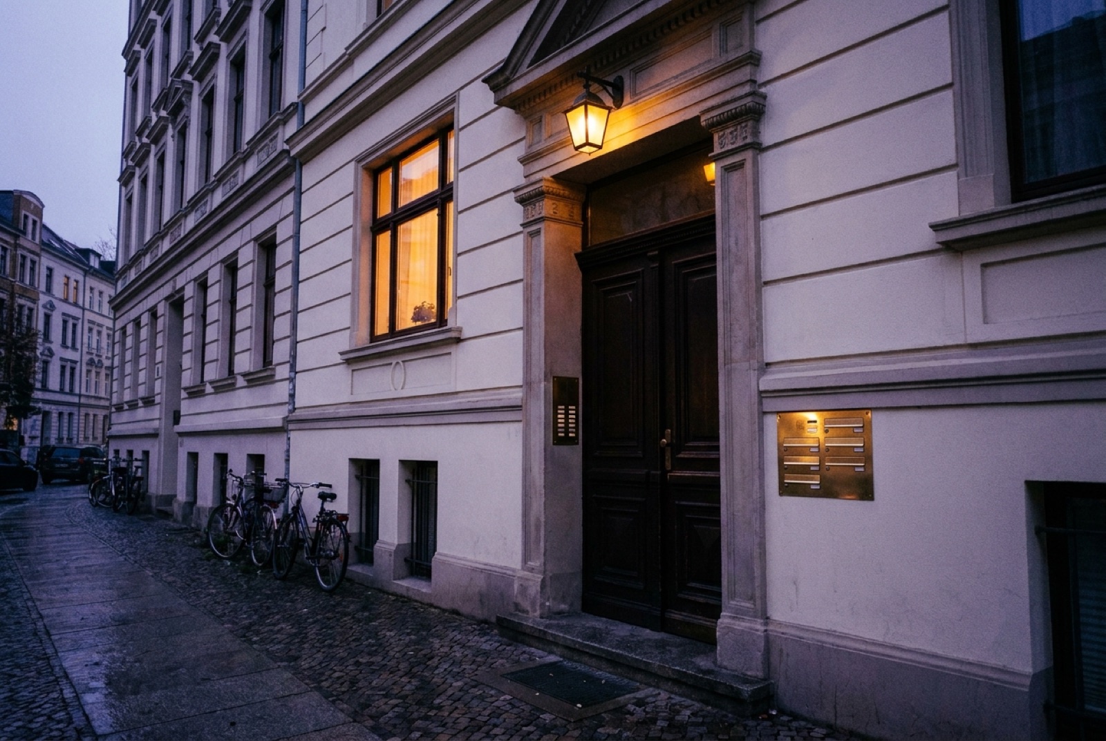 Haustür eines Gründerzeithauses in der Dämmerung, Klingelschild leuchtet warm, ein Fenster erleuchtet