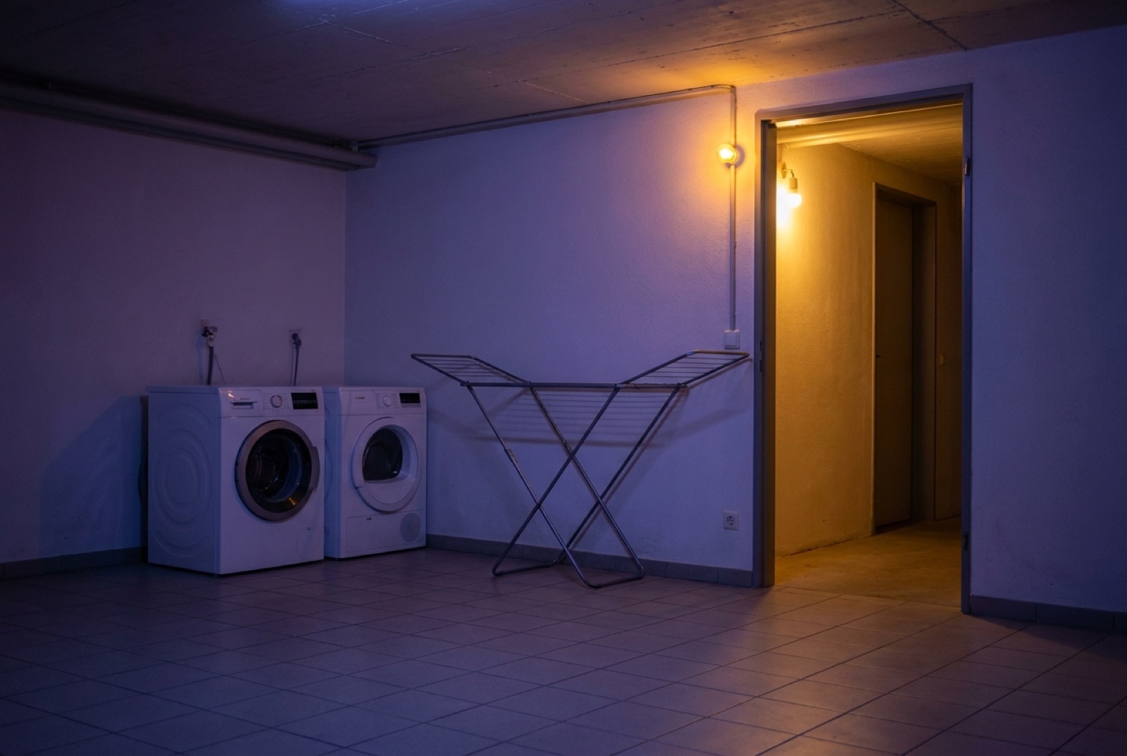 Gemeinschaftliche Waschküche im Keller, warmes Licht fällt aus dem Gang herein